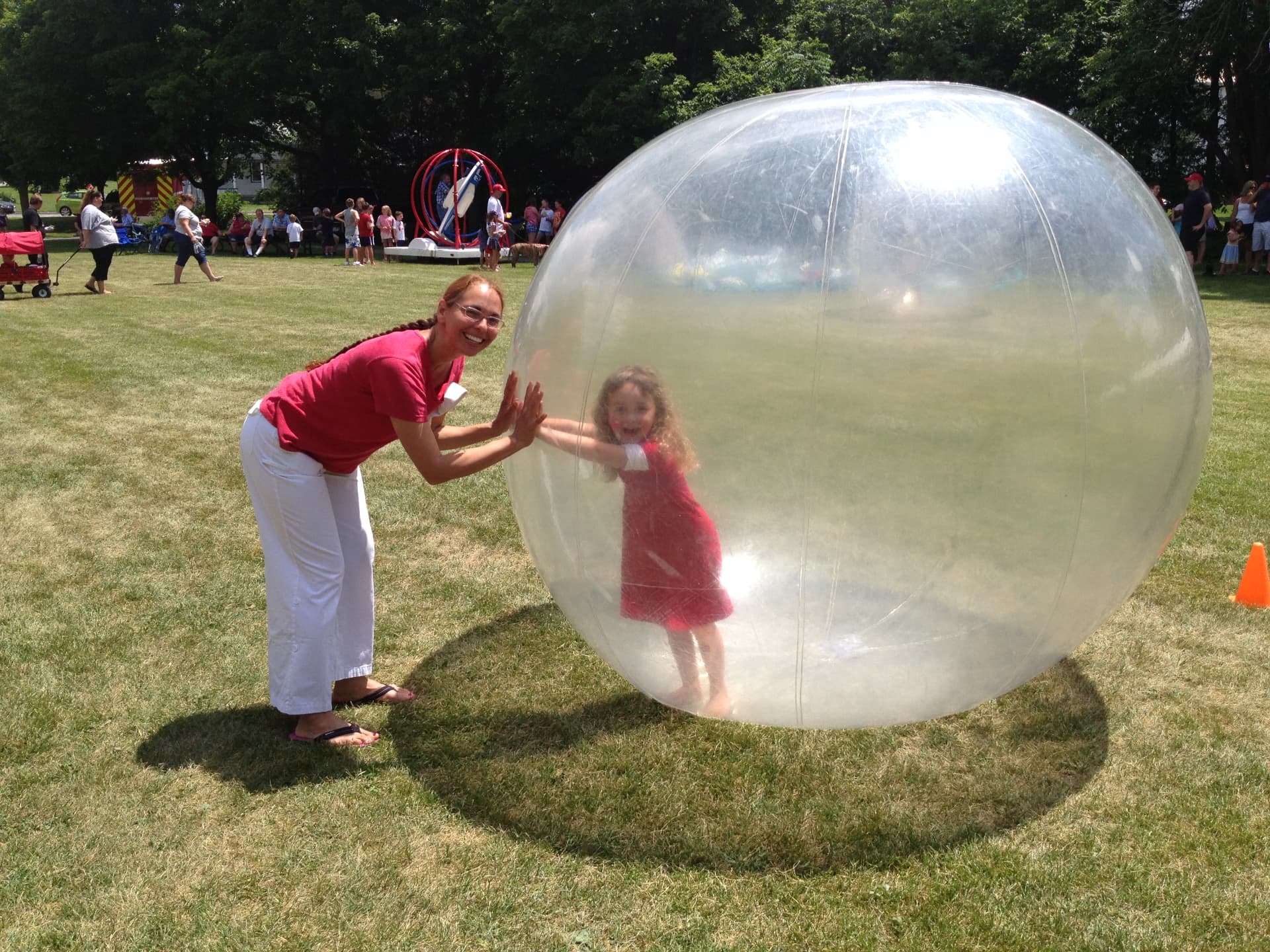 A mother and young child playing with a large inflatable ball at a community event in a Warkworth park